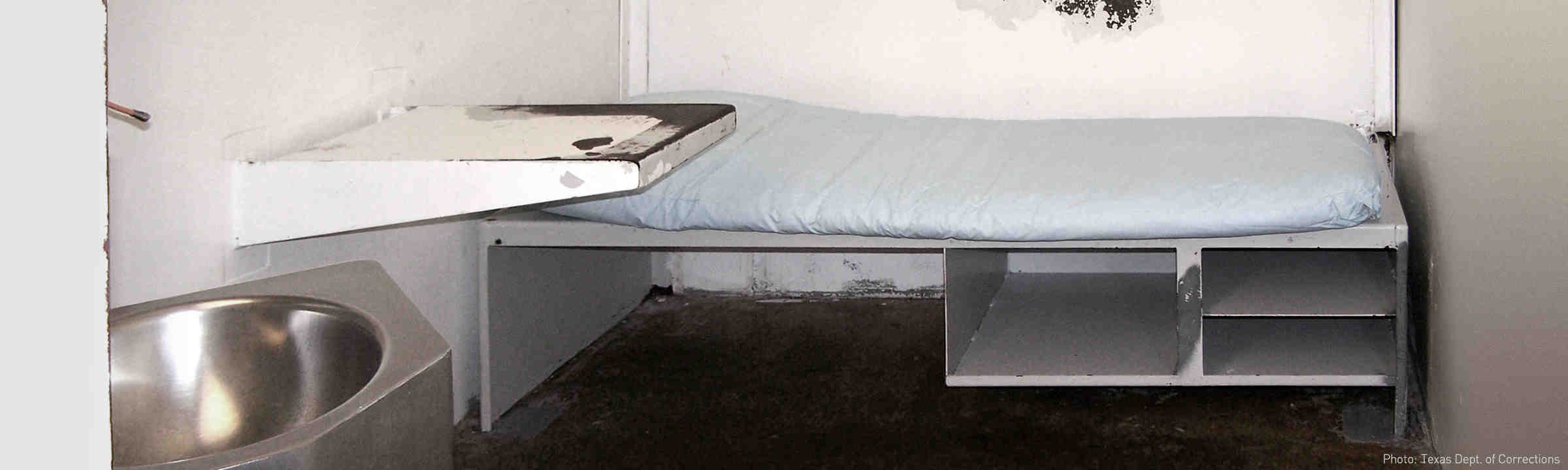 An empty bed and sink within a jail cell.