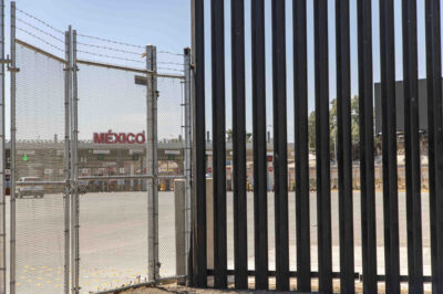 Tall border fence with a "México" sign in the background