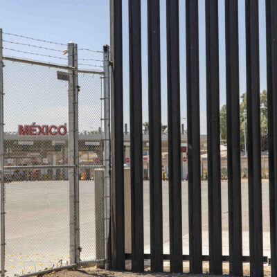 Tall border fence with a "México" sign in the background