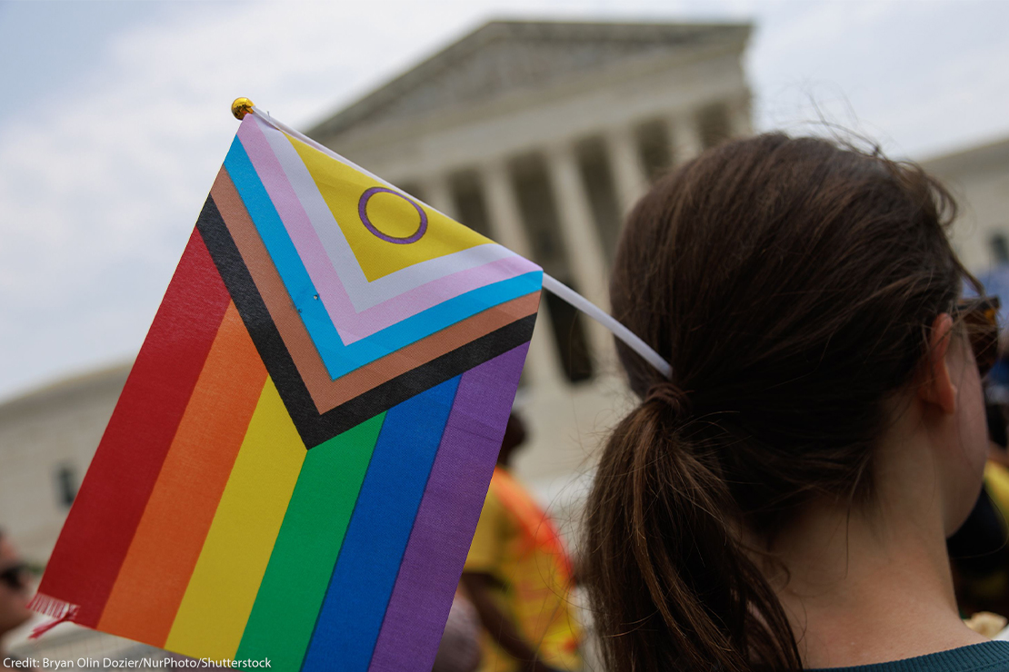 A Pride supporter (whose face cannot be seen) holds an Intersex-inclusive Pride Flag in their hair while facing the Supreme Court.