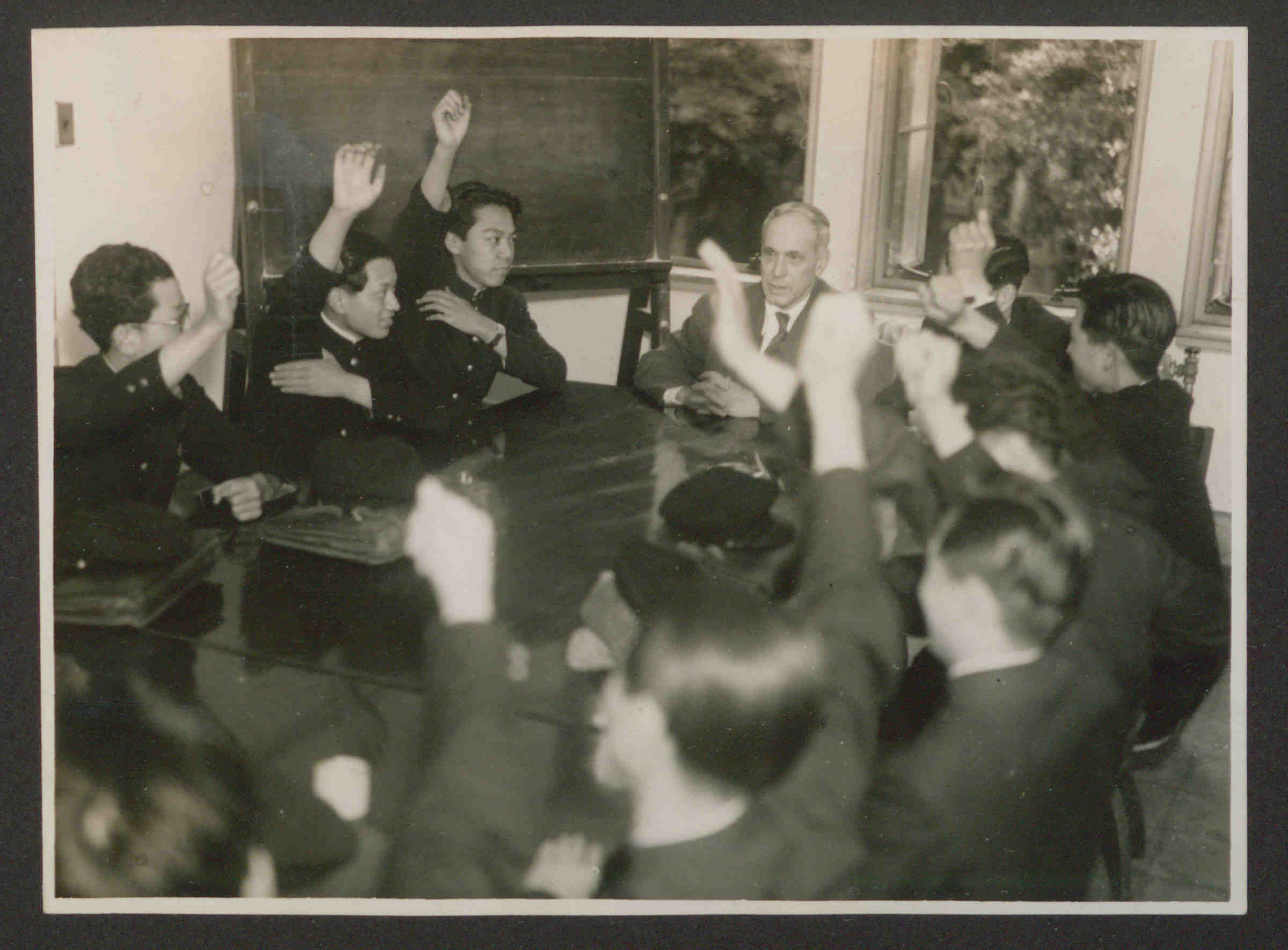 Roger N. Baldwin sitting at a table surrounded by many students with raised hands