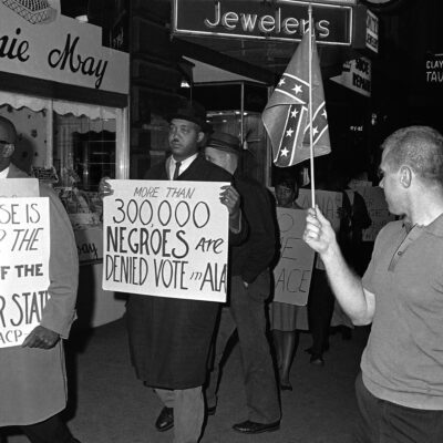 Demonstrators march past a man holding a Confederate flag.