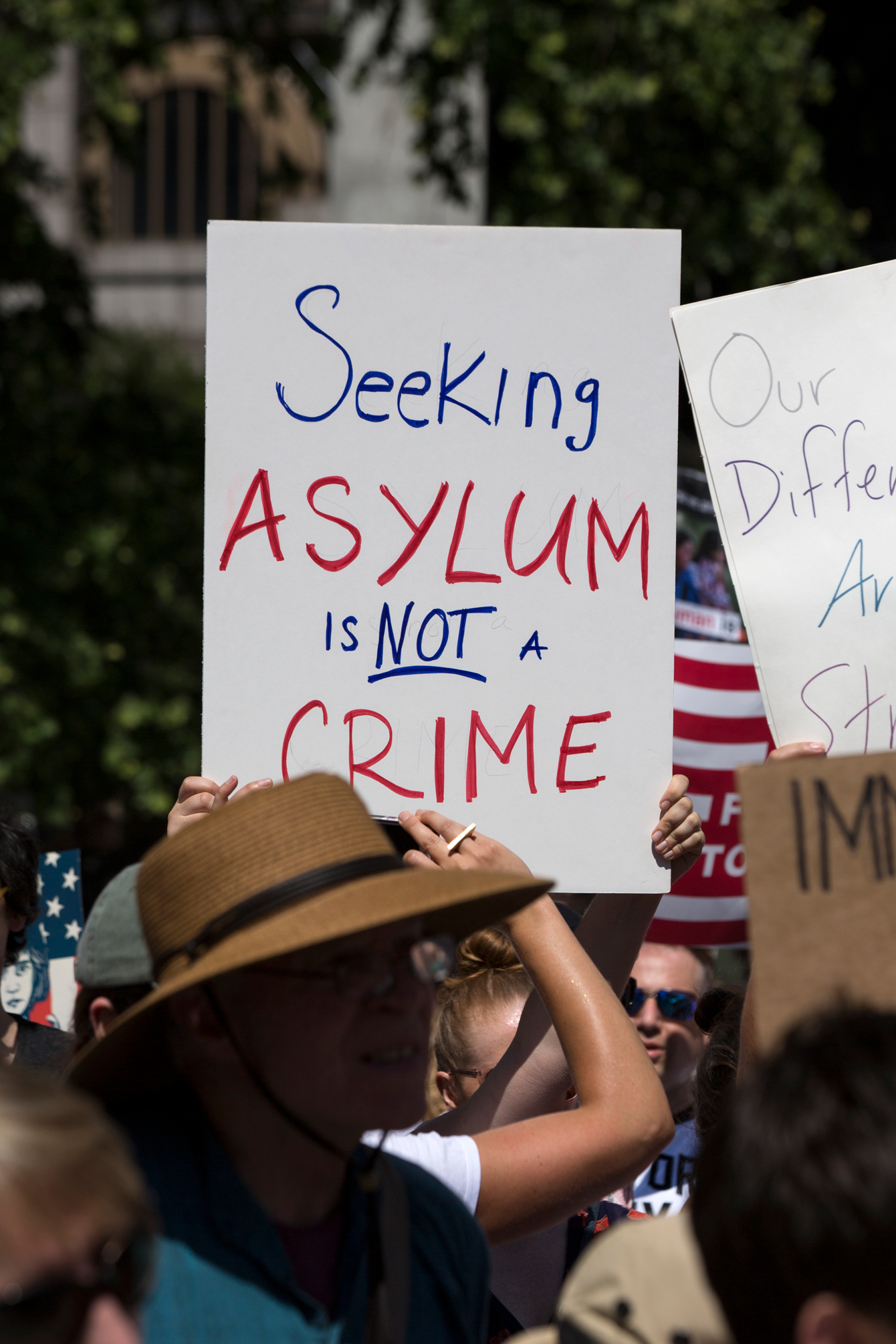 A protestor holding a sign that reads "Seeking Asylum Is Not A Crime"