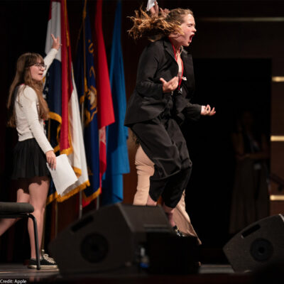 Cecilia Bartin jumping on stage in "Girls State," now streaming on Apple TV+.