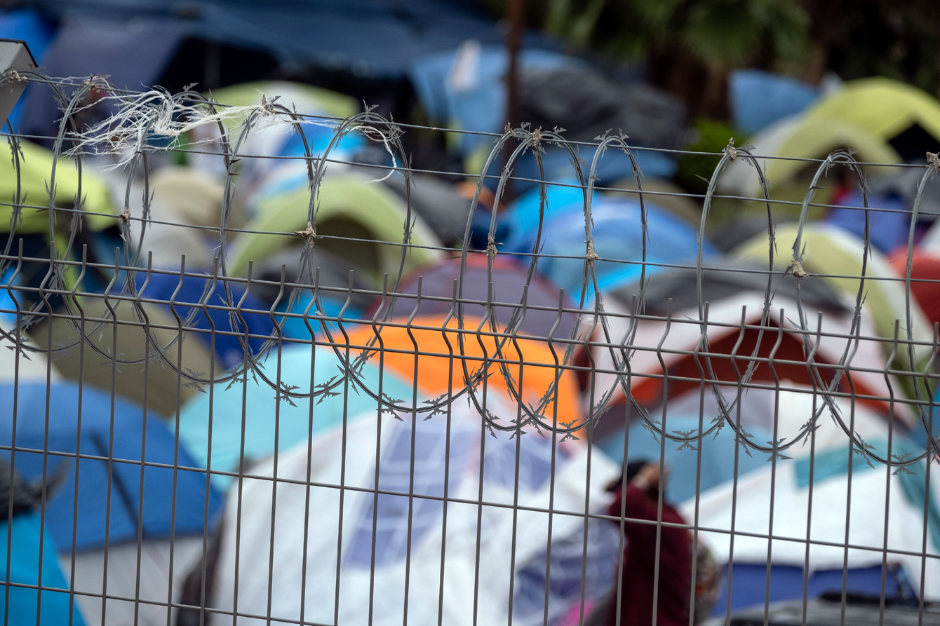 A barbed wire topped fence in front of an encampment