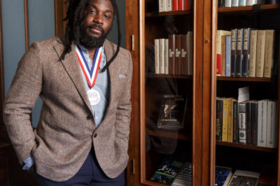 Jason Reynolds, National Ambassador for Young People’s Literature, 2020-2022. Stands in front of a bookshelf.