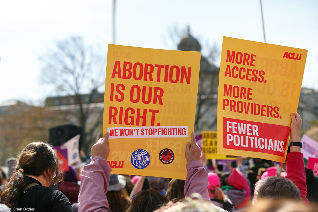 A demonstrator holds up a poster eading "ABORTION IS OUR RIGHT, WE WON'T STOP FIGHTING" while another holds a poster reading "MORE ACCESS. MORE PROVIDERS. FEWER POLITICIANS." as others protest the proposed limited use of mifepristone outside the U.S. Supreme Court on the 26th of March 2024.