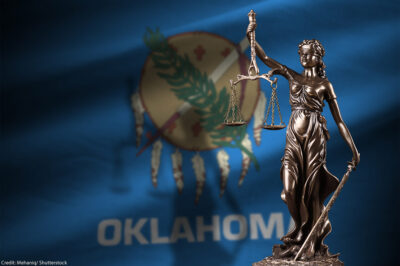 The justice statue in front of the Oklahoma state flag.