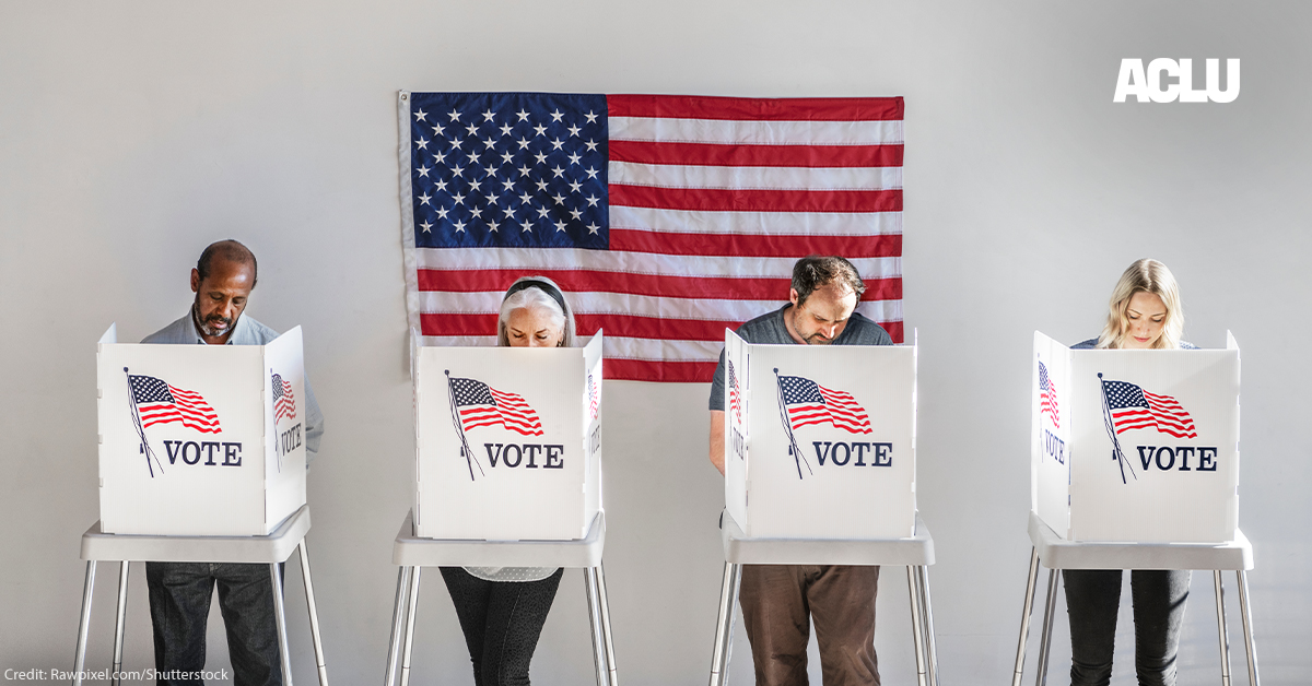 With and American flag in the background, four people in the act of voting, stand behind voter booths as they make their selections.