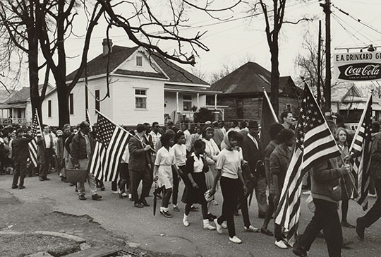 A historical image of many people marching, some holding American flags