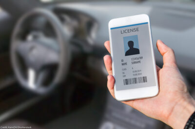 A hand (within a car) holding a cellphone displaying a digital drivers license.