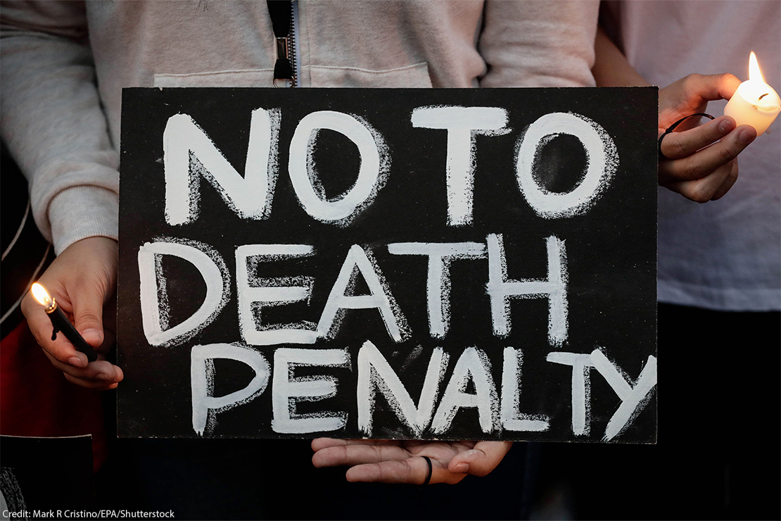 Two pairs of hands holding a lit lighter and candle as well as a sign reading "NO TO DEATH PENALTY".