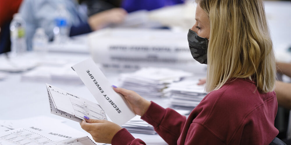 A woman with a surgical mask opening absentee ballots.