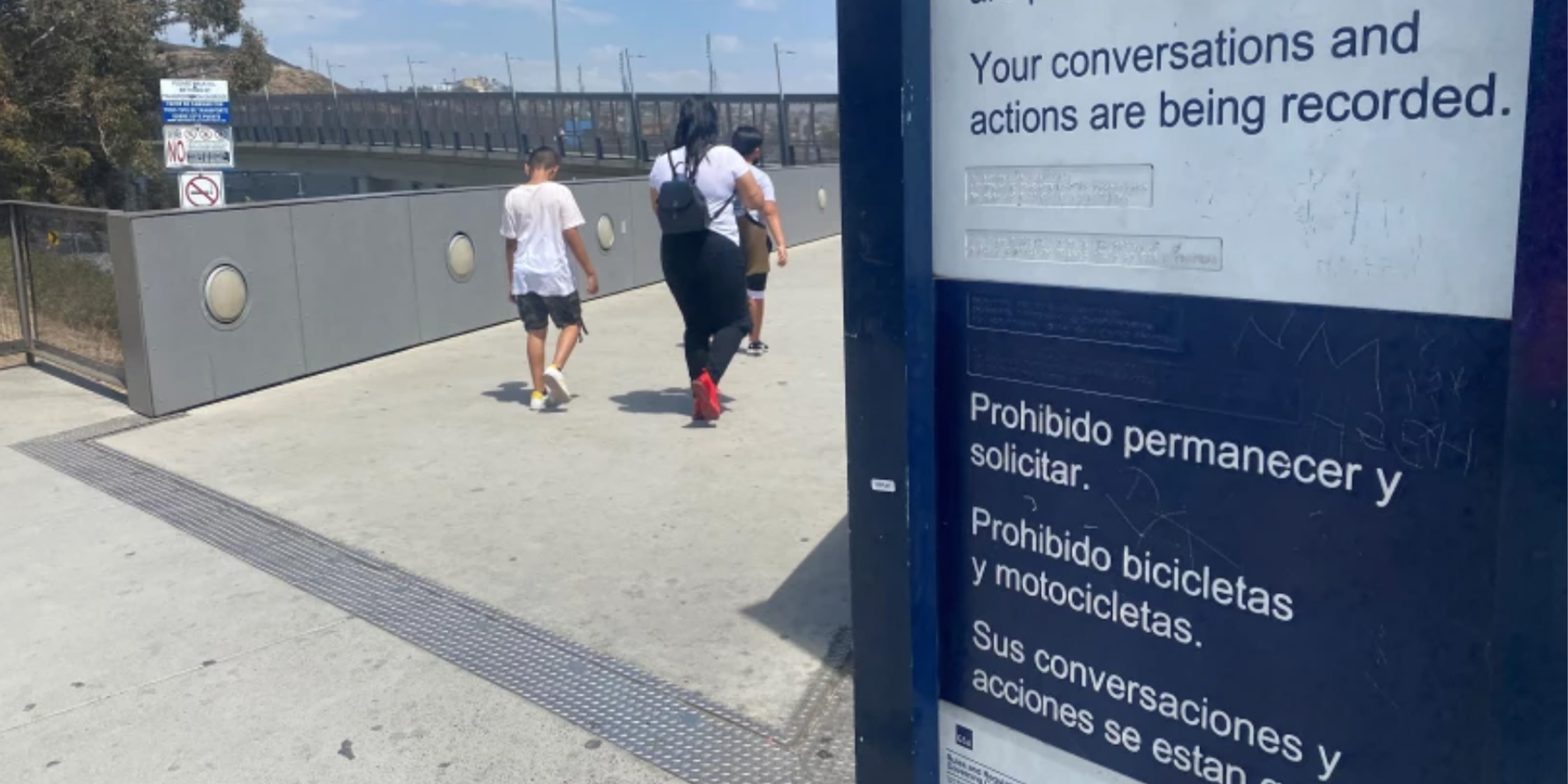 Immigrants arriving at an in intake shelter walk by signs stating that their conversations are being recorded.