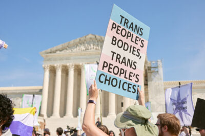 A demonstrator at a march in front of the Supreme Court holds up a sign reading "TRANS PEOPLE'S BODIES, TRANS PEOPLE'S CHOICES".