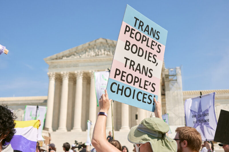 A demonstrator at a march in front of the Supreme Court holds up a sign reading "TRANS PEOPLE'S BODIES, TRANS PEOPLE'S CHOICES".