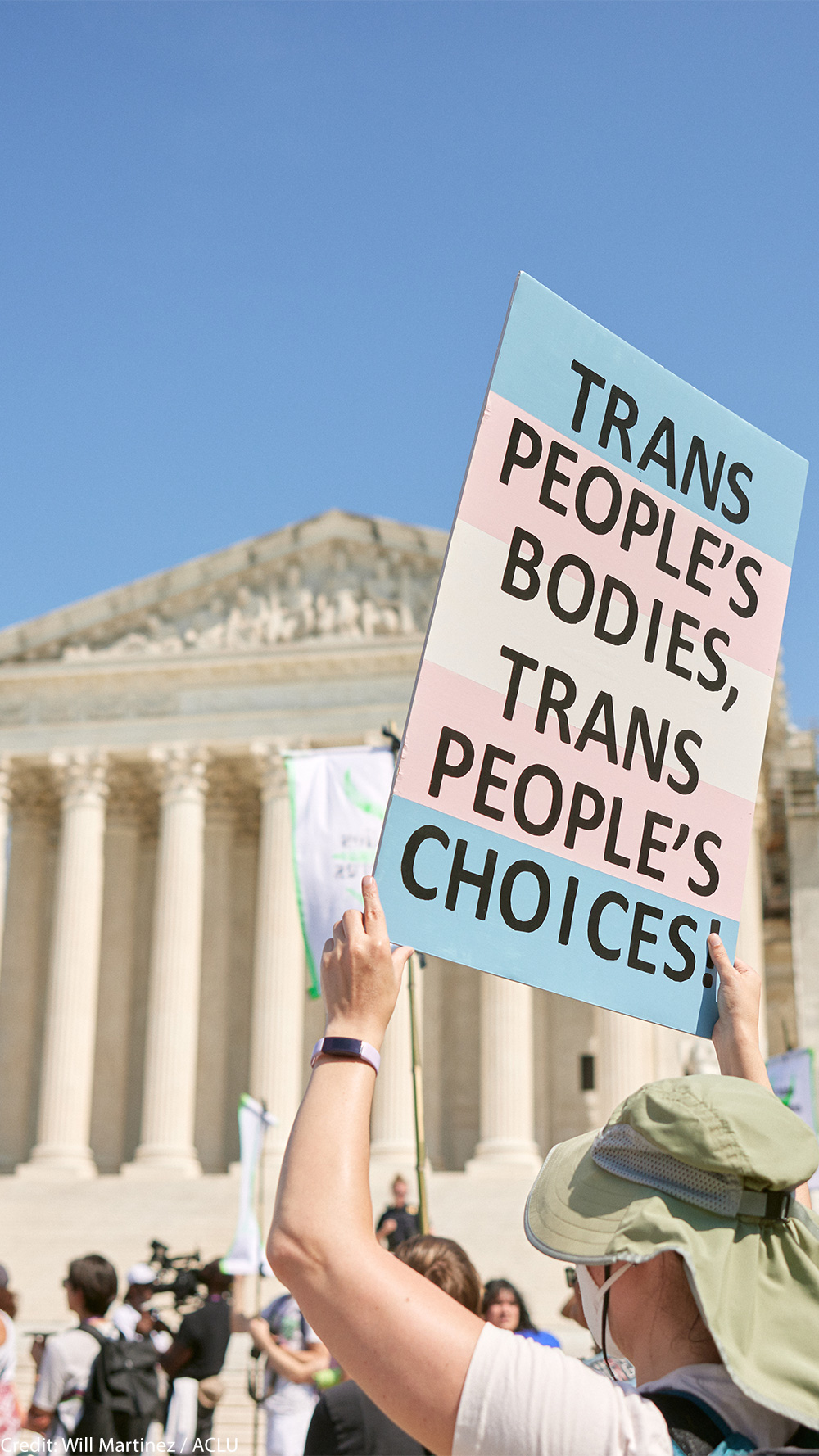 A demonstrator at a march in front of the Supreme Court holds up a sign reading "TRANS PEOPLE'S BODIES, TRANS PEOPLE'S CHOICES".