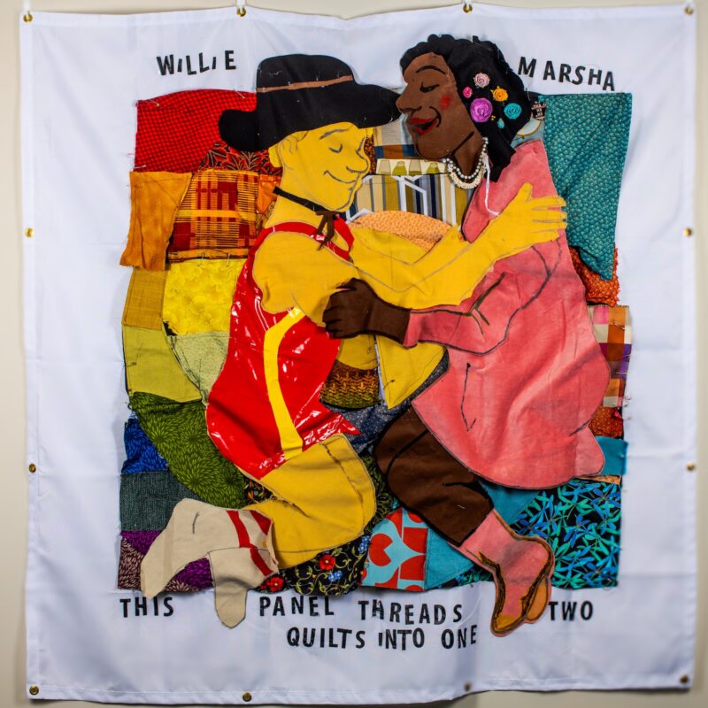 Trans icon Marsha P. Johnson lays on a half AIDS Quilt / half Freedom To Be quilt with roommate and chosen family Little Brave, William Brashear.