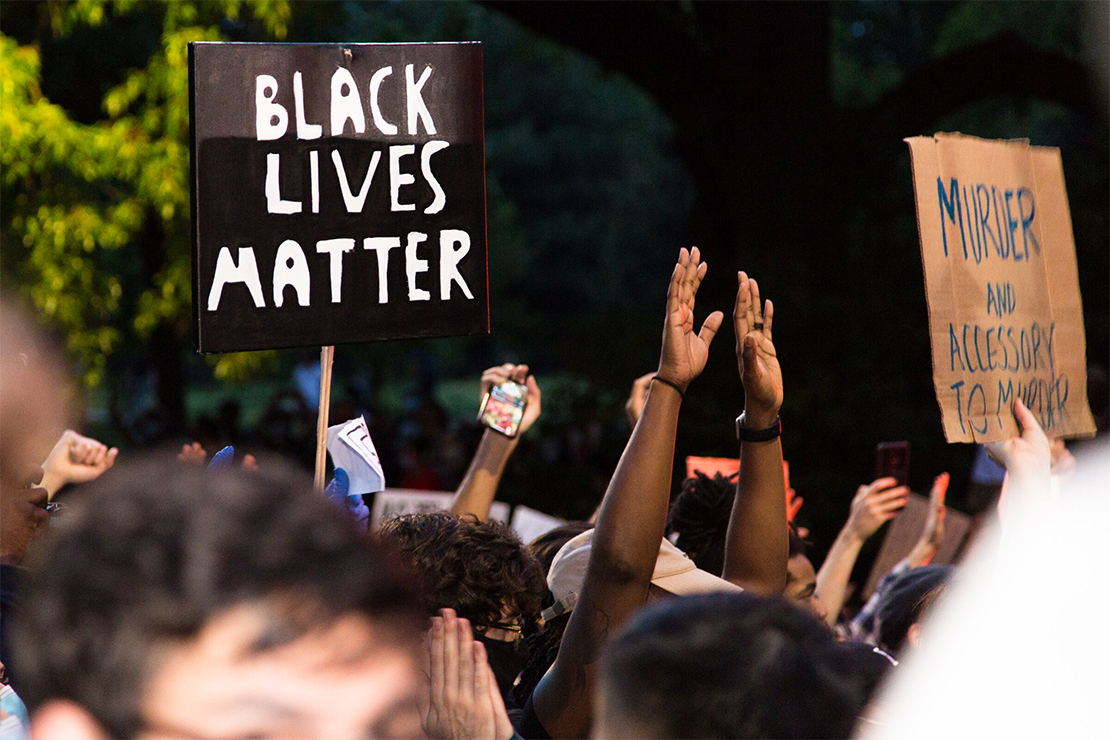 With only their arms visible, protestors march with hands in the air carrying signs that read "BLACK LIVES MURDER" and "Murder and Accessory to Murder."