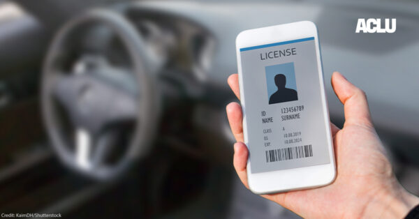 A hand is holding a mobile phone with a mockup of a digital license on it, with a car steering wheel in the background