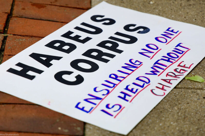 A sign reading " HABEAS CORPUS Ensuring No One is Held Without Charge" lying on the ground.