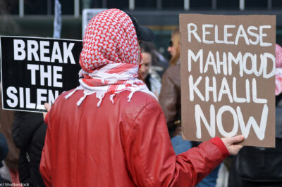 A student activist holding a sign that says "Release Mahmoud Khalil Now."
