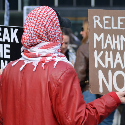 A student activist holding a sign that says "Release Mahmoud Khalil Now."