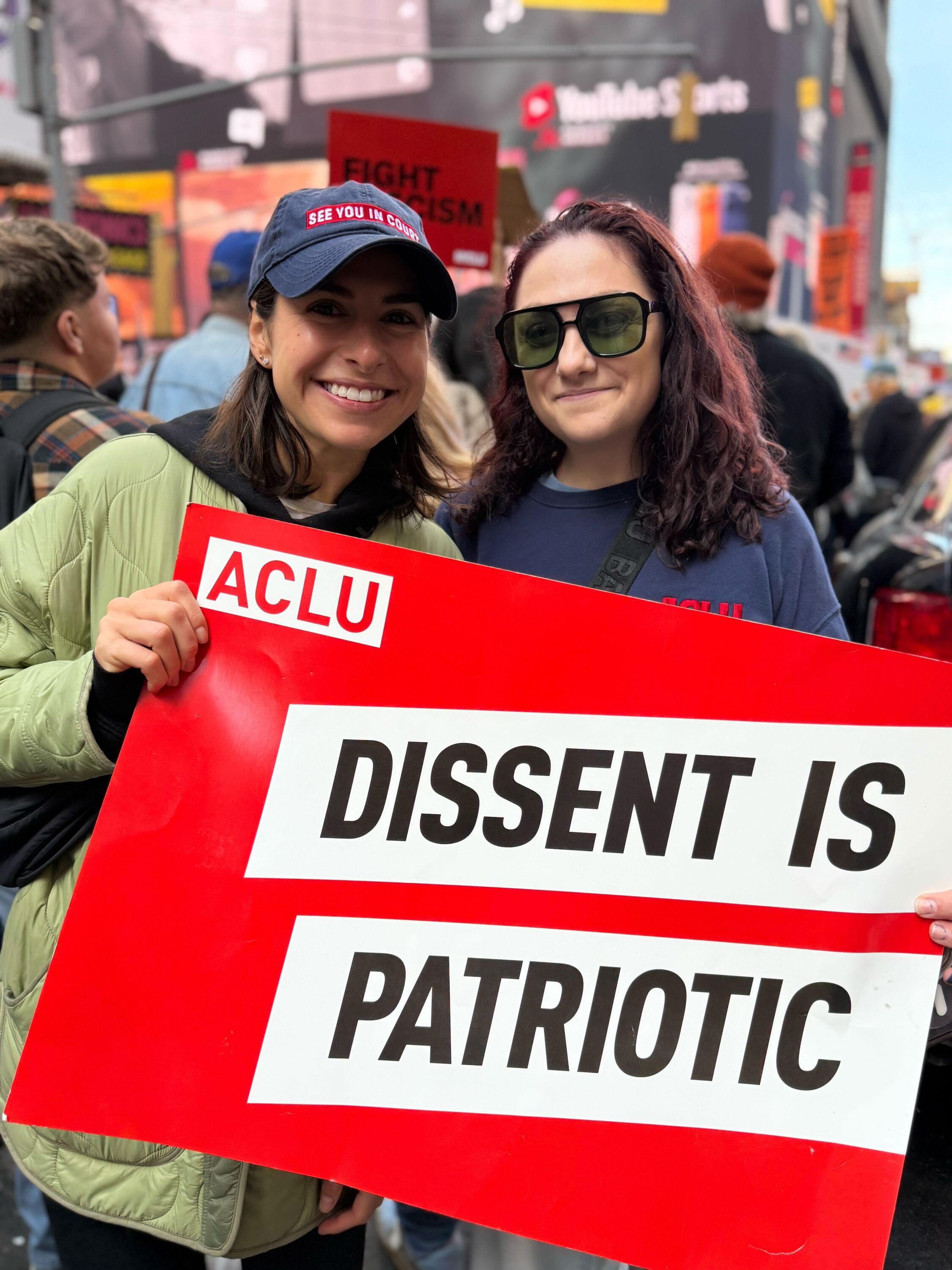 Two women hold up an Ƶ placard which reads "Dissent is Patriotic"