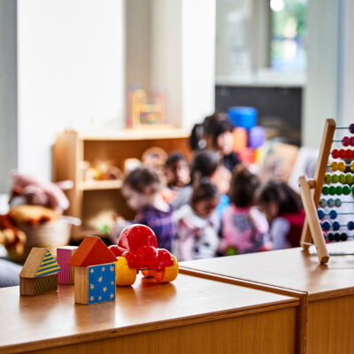 Toys in the forefront and preschoolers (blurred out) in class in the background.