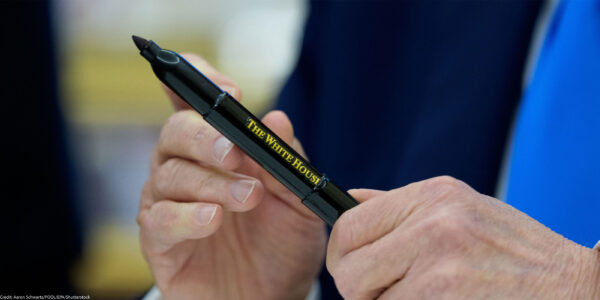 A close-up of President Trump’s hands holding a black marker pen inscribed with “The White House” in gold lettering, moments after signing executive orders in the Oval Office.