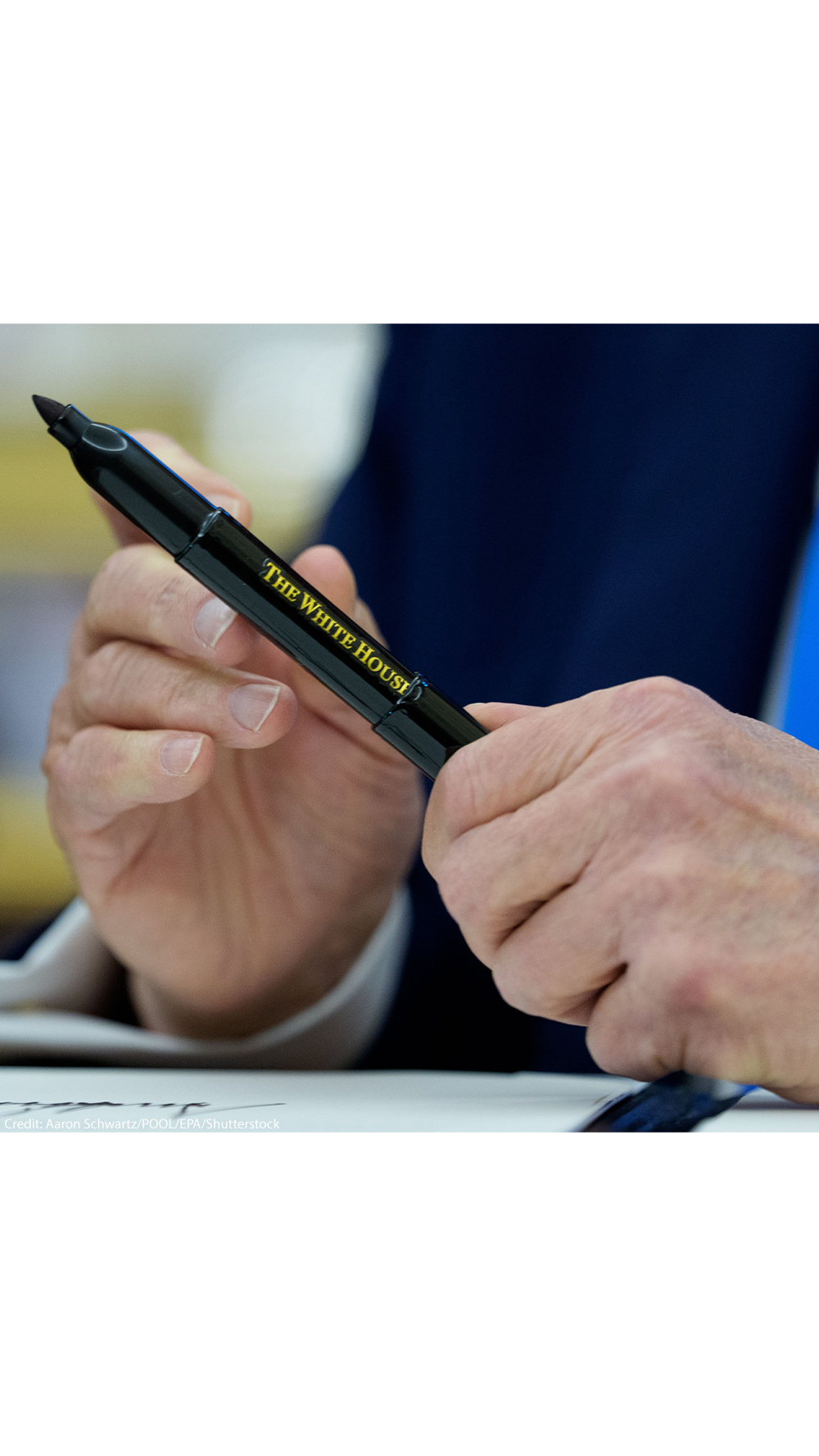 A close-up of President Trump’s hands holding a black marker pen inscribed with “The White House” in gold lettering, moments after signing executive orders in the Oval Office.