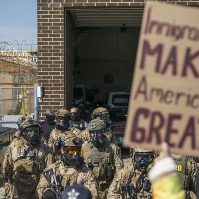 Heavily armed ICE and Border Patrol agents guard the Broadview ICE facility from peaceful protesters opposed to 'Operation Midway Blitz' in Chicagoland; their sign reads 'Immigrants Make America Great'