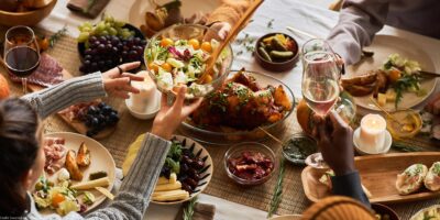 A multi-ethnic group of people sharing a festive, communal meal at a dining table with roasted chicken, salad, bread, fruit, and wine.