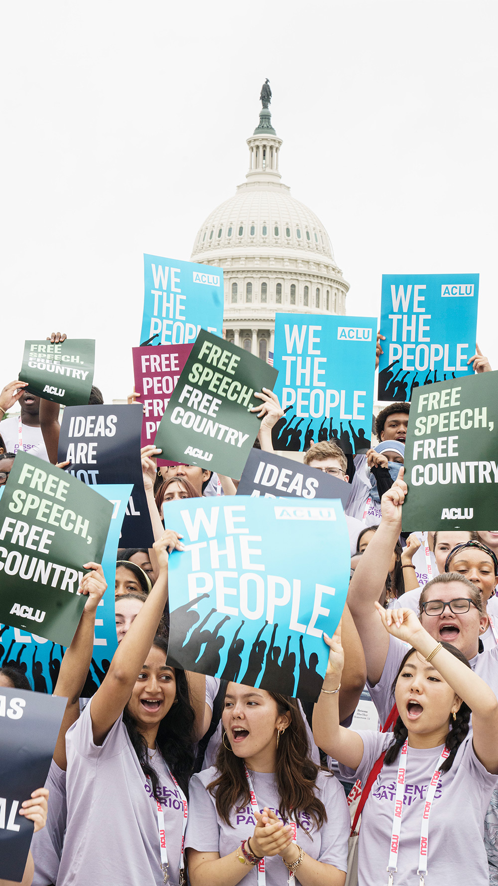A large group of students in the ACLU’s National Advocacy Institute, stand in front of the U.S. Capitol, cheering and holding signs that read “We the People,” “Free Speech, Free Country,” and “Ideas Are Not Illegal.”