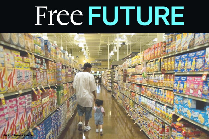 A man holding a child's hand and walking down a colorful grocery store aisle