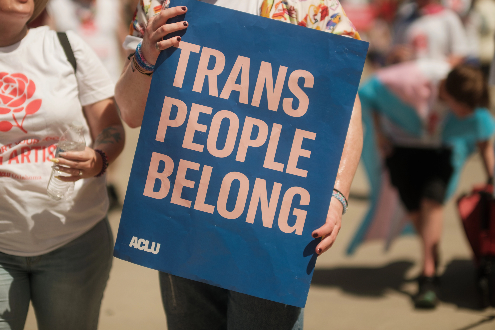 A protestor holds a sign that says Trans People Belong.