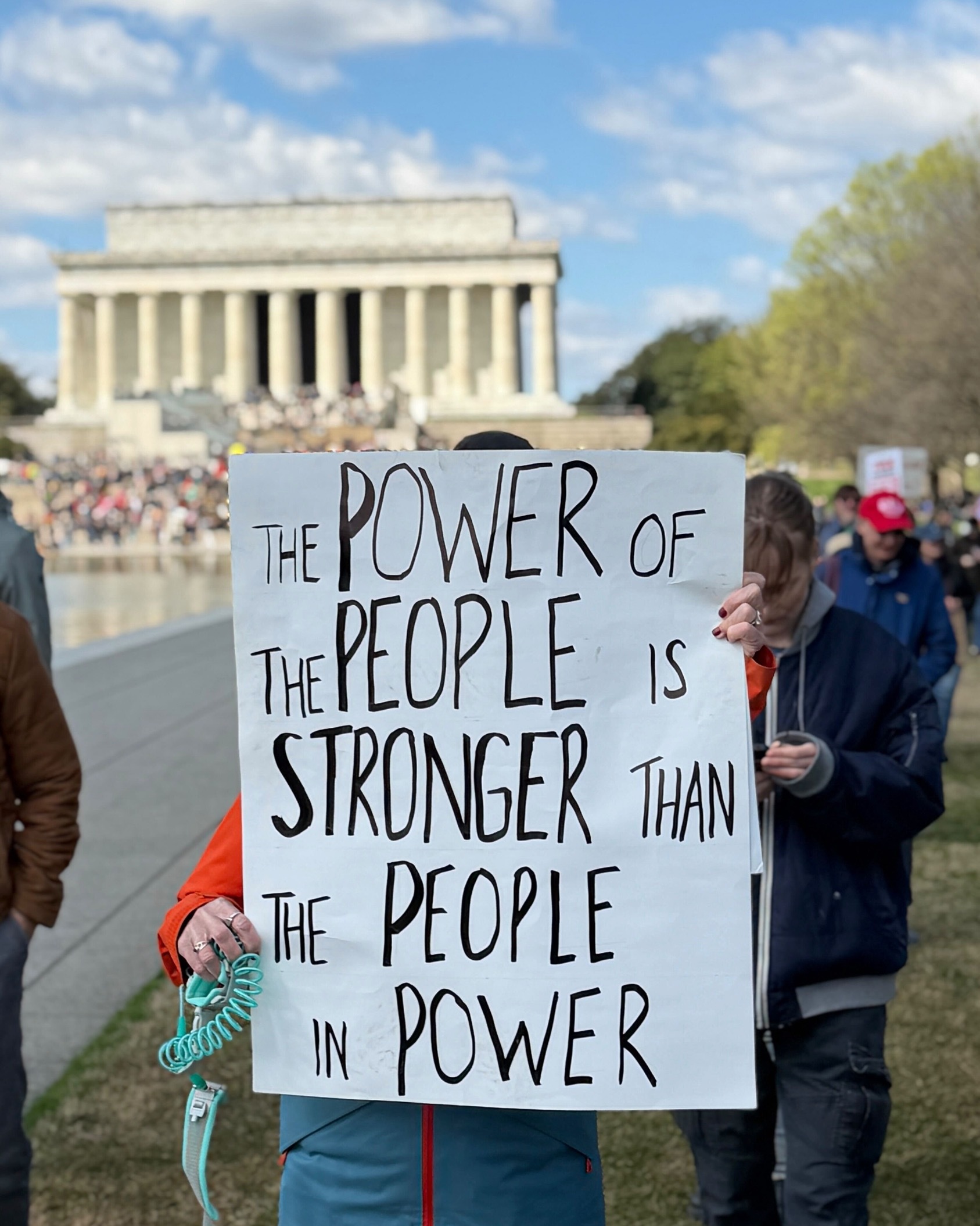 A protestor holds a sign that says The Power of the People is Stronger than the People in Power