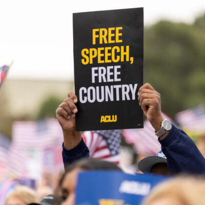 A protestor holds a sign that says Free Speech, Free Country
