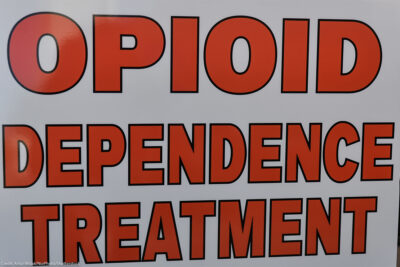 Close-up of a sign reading “OPIOID DEPENDENCE TREATMENT” in large red letters on a white background.