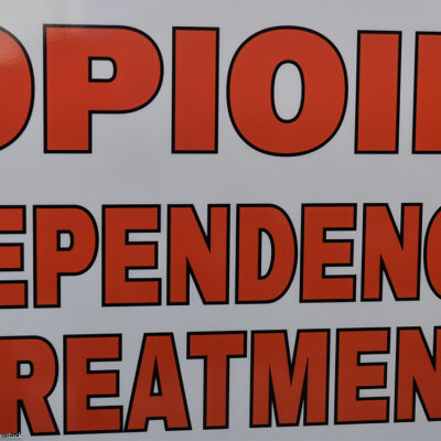 Close-up of a sign reading “OPIOID DEPENDENCE TREATMENT” in large red letters on a white background.