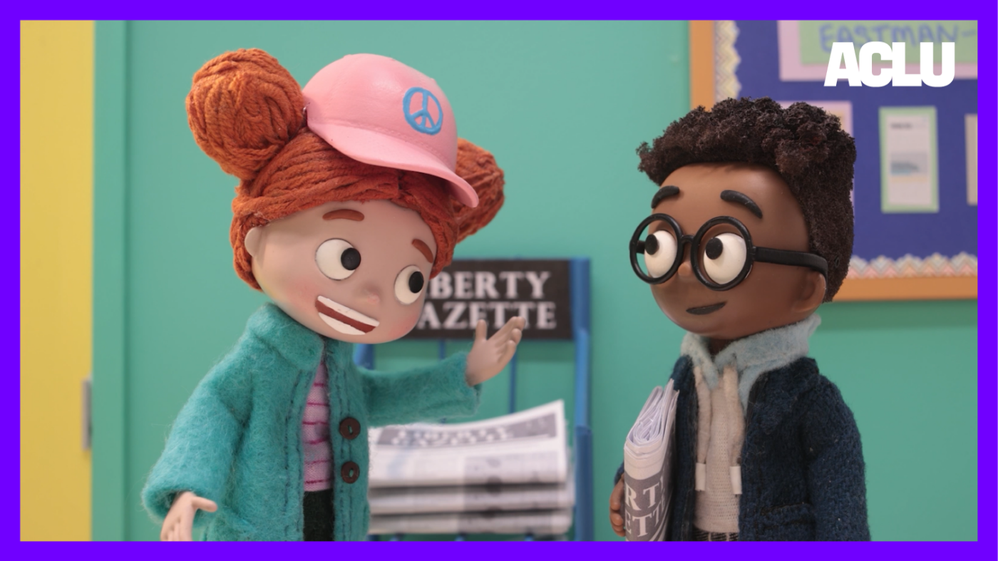 A still frame from episode 1: Lisa is talking to Aaron in front of a rack holding the school newspaper.