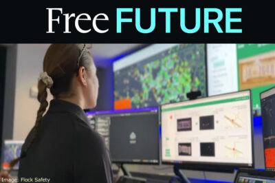 A police officer looking at a wall full of screens in a crime center showing maps and data