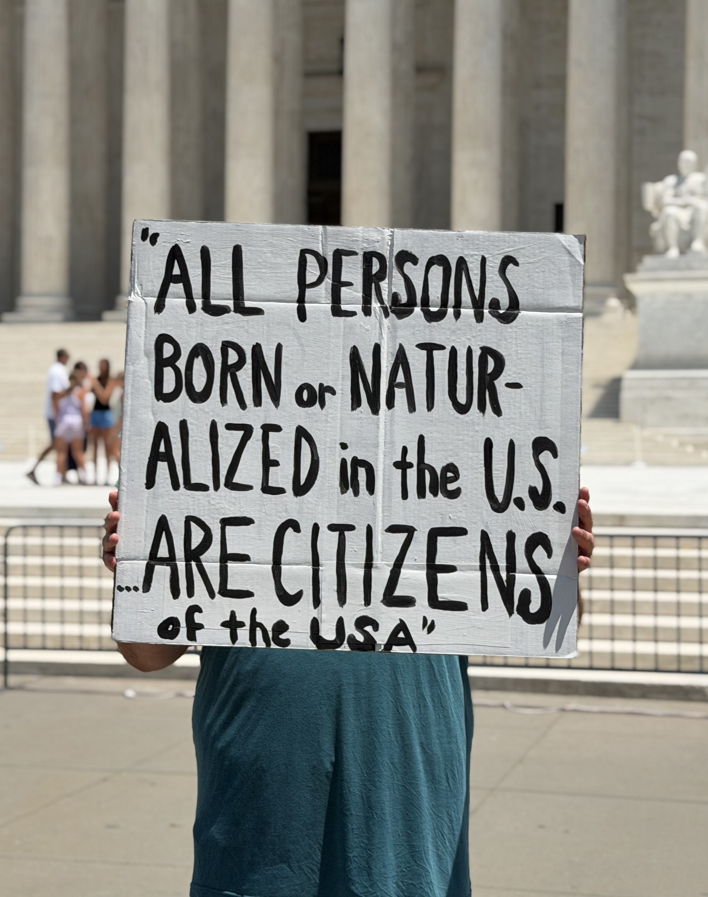 A person holds a handmade sign that says All persons born or naturalized in the U.S. are citizens of the USA.