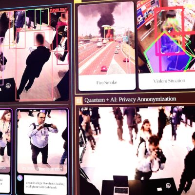 Large display showing an AI security surveillance dashboard using facial recognition-style tracking, with colored boxes around people in CCTV footage and labeled panels for "Advanced Search/Alarm," "Anomaly Analytics" (fire/smoke, violent situation, fall detection), and "Privacy Anonymization."