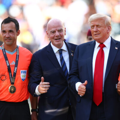 FIFA President Gianni Infantino and President Donald Trump pose with FIFA officials in bright orange referee jerseys and medals during the awards ceremony after Chelsea defeated Paris Saint-Germain 3–0 in the 2025 FIFA Club World Cup final at MetLife Stadium in East Rutherford, New Jersey.