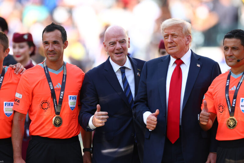 FIFA President Gianni Infantino and President Donald Trump pose with FIFA officials in bright orange referee jerseys and medals during the awards ceremony after Chelsea defeated Paris Saint-Germain 3–0 in the 2025 FIFA Club World Cup final at MetLife Stadium in East Rutherford, New Jersey.