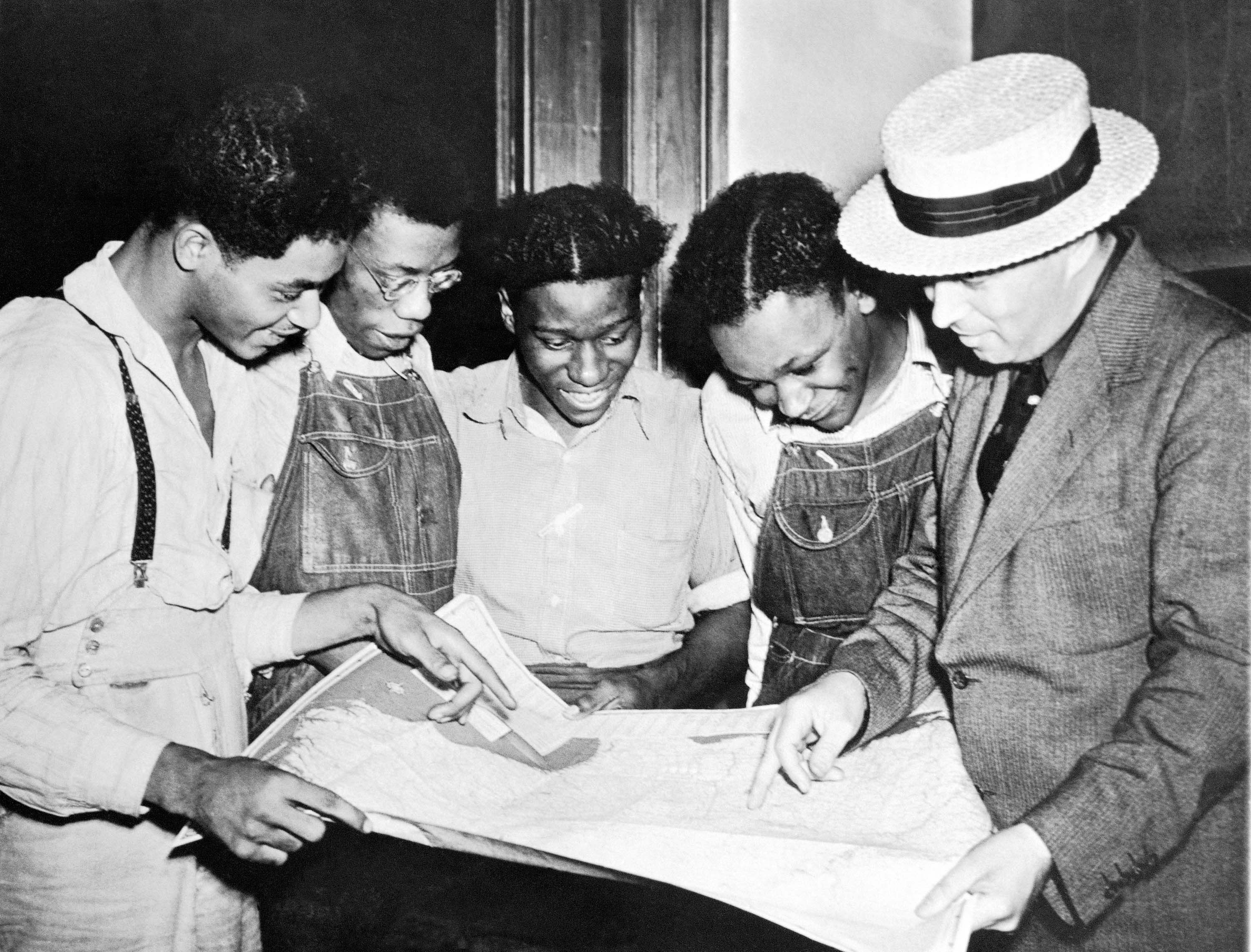 Black and white photo of the Scottsboro Case defendants and lawyer consulting a case document