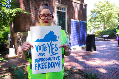 A photo of Heather St. Amand holding a sign that says "Vote Yes on Reproductive Freedom."