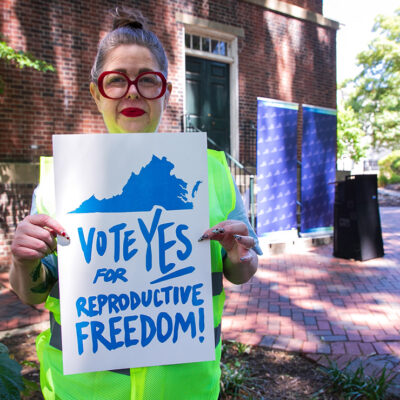 A photo of Heather St. Amand holding a sign that says "Vote Yes on Reproductive Freedom."