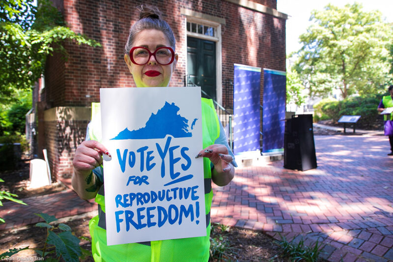 A photo of Heather St. Amand holding a sign that says "Vote Yes on Reproductive Freedom."